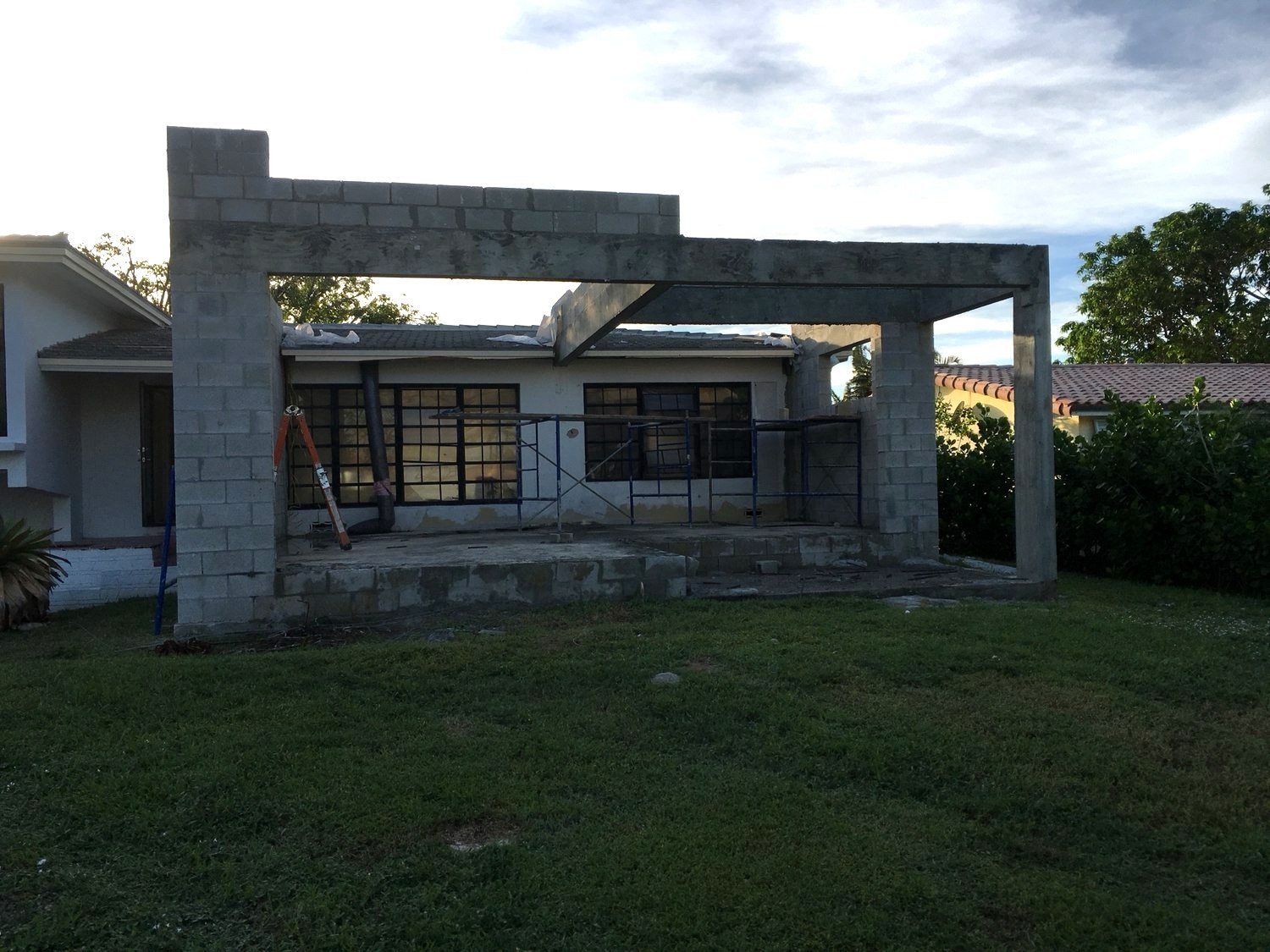 Concrete block walls of a new flat-roof addition rising in front of the existing single-story house