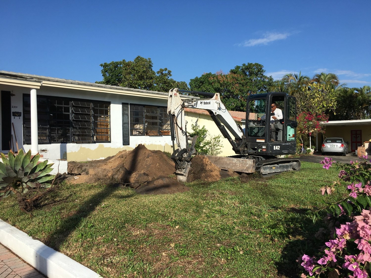 Compact excavator working in the front yard during sitework