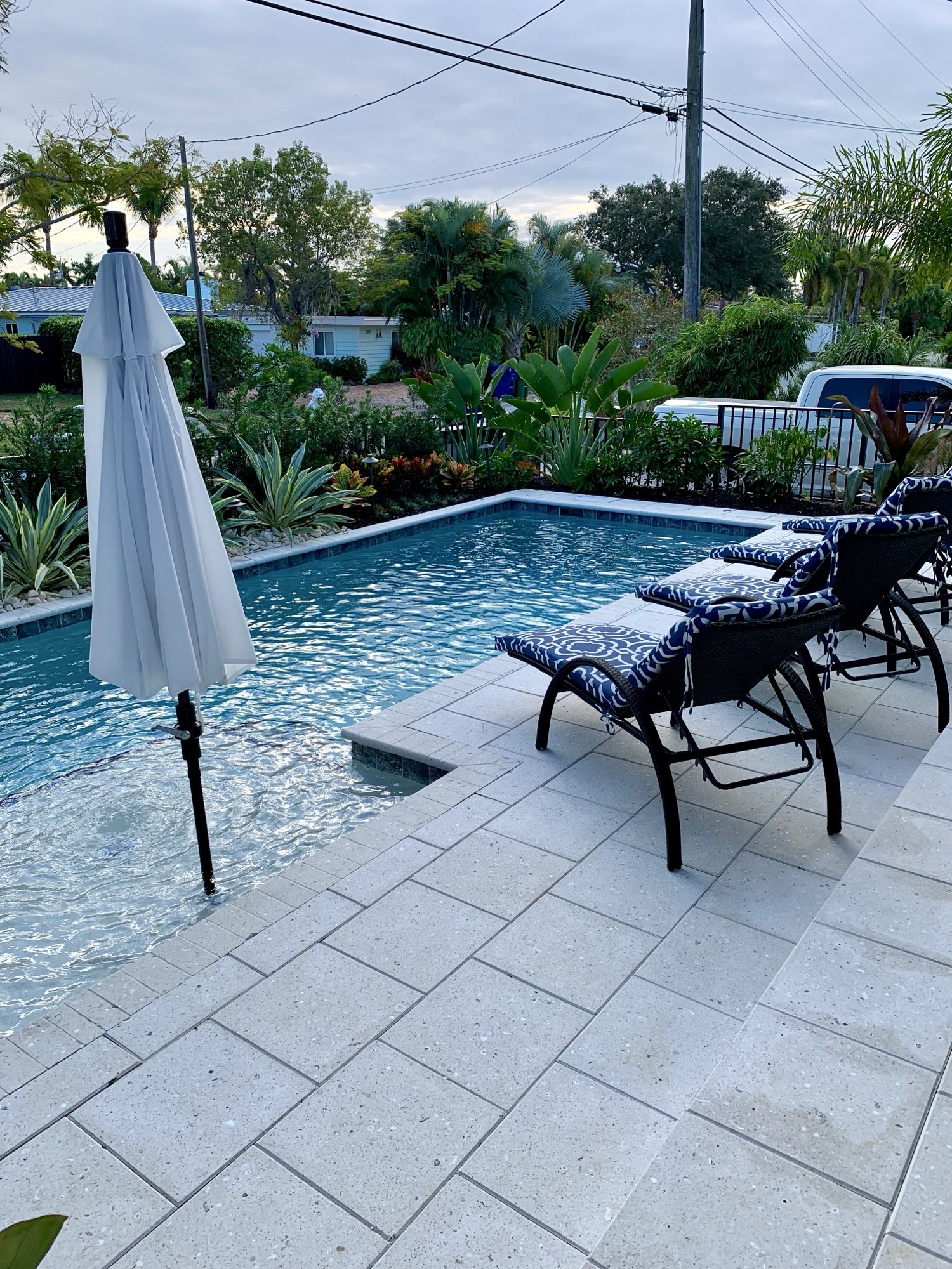 Finished stone pool deck with loungers and an umbrella beside the water