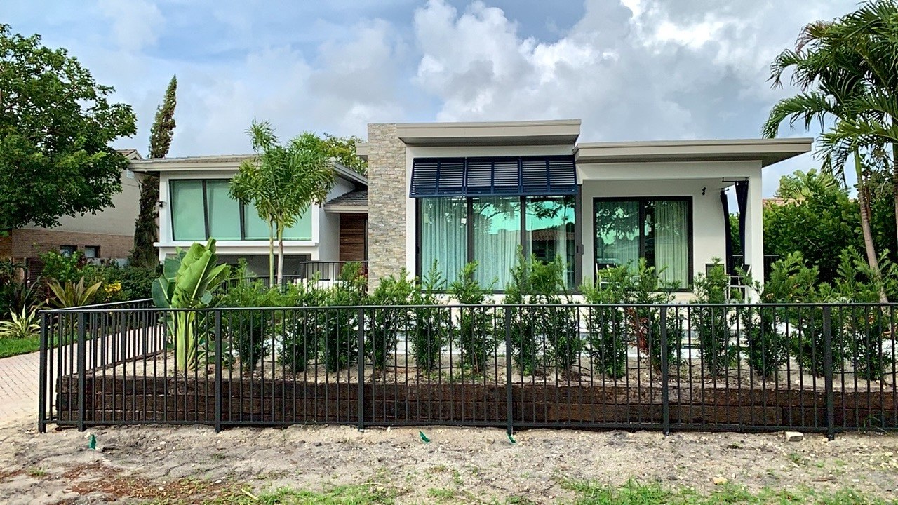 Completed flat-roof addition seen straight on from the street, with stone-clad column, black-framed glass, a metal awning and new landscaping behind an aluminium fence