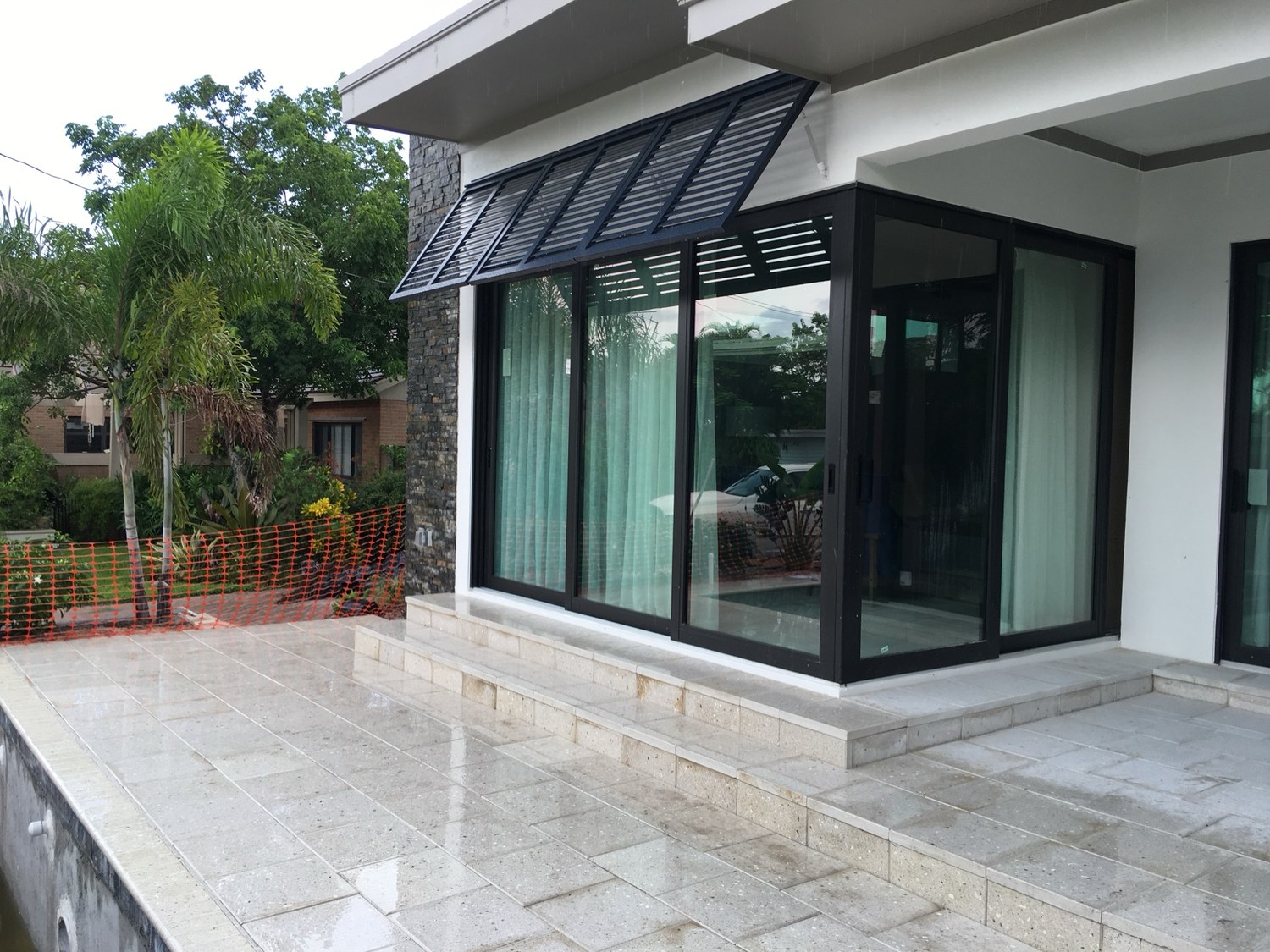 Corner of the finished addition with floor-to-ceiling black-framed glass opening onto the stone deck