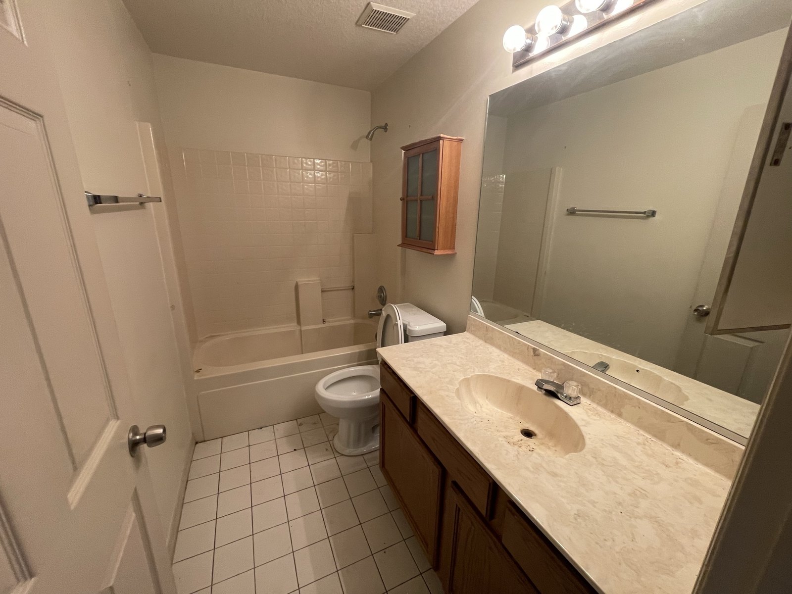 The same guest bathroom before renovation, with dated tile, a cultured marble vanity top and oak cabinets