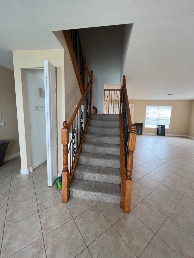 The same staircase before renovation, with carpeted treads, an oak handrail and wrought-iron balusters over tile flooring