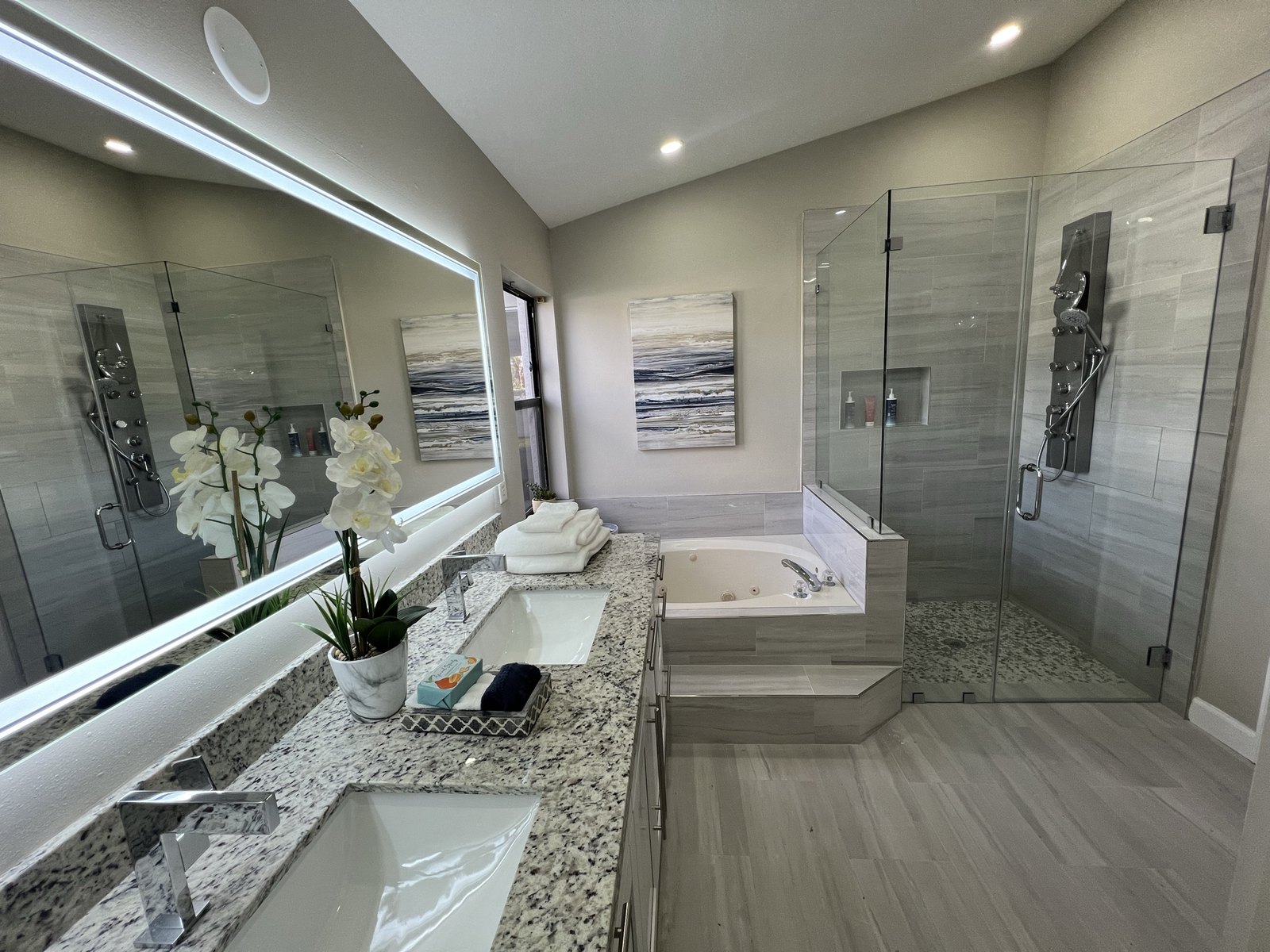 Completed master bathroom with a double granite vanity, backlit mirror, corner soaking tub and frameless glass shower
