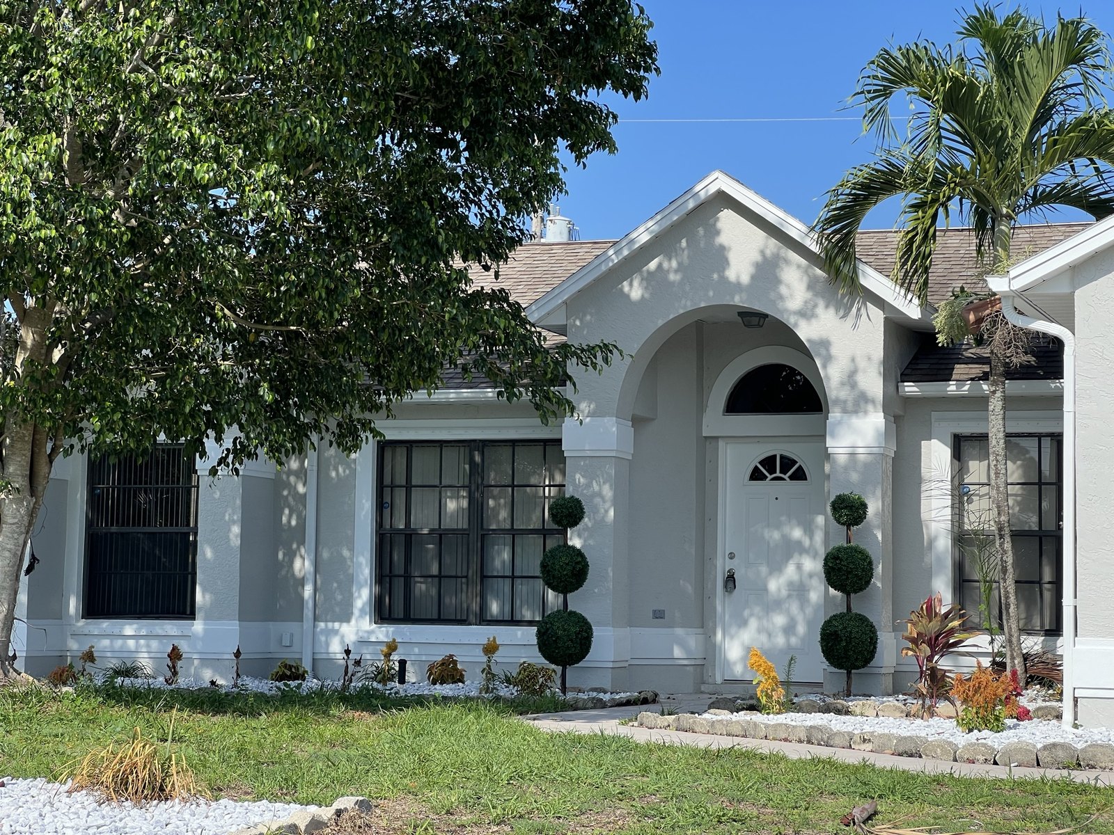 Completed exterior with fresh white stucco, new landscaping, topiaries and a white rock border