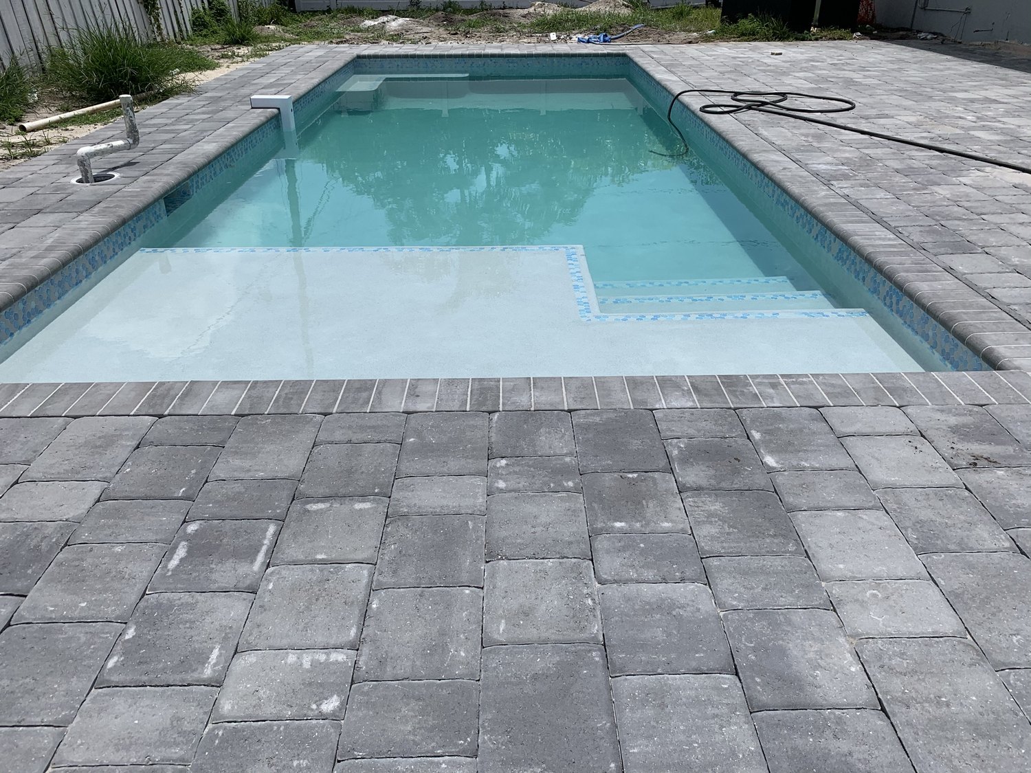 Finished pool filled with water alongside the new paver deck