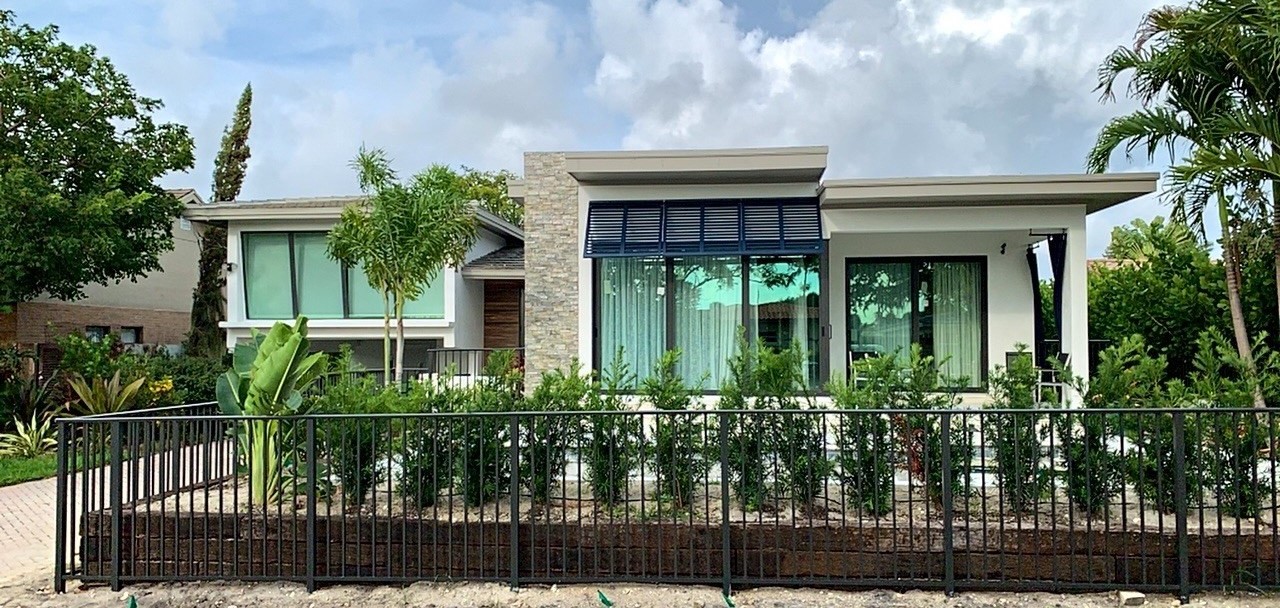 Completed flat-roof addition seen straight on from the street, with stone-clad column, black-framed glass, a metal awning and new landscaping behind an aluminium fence
