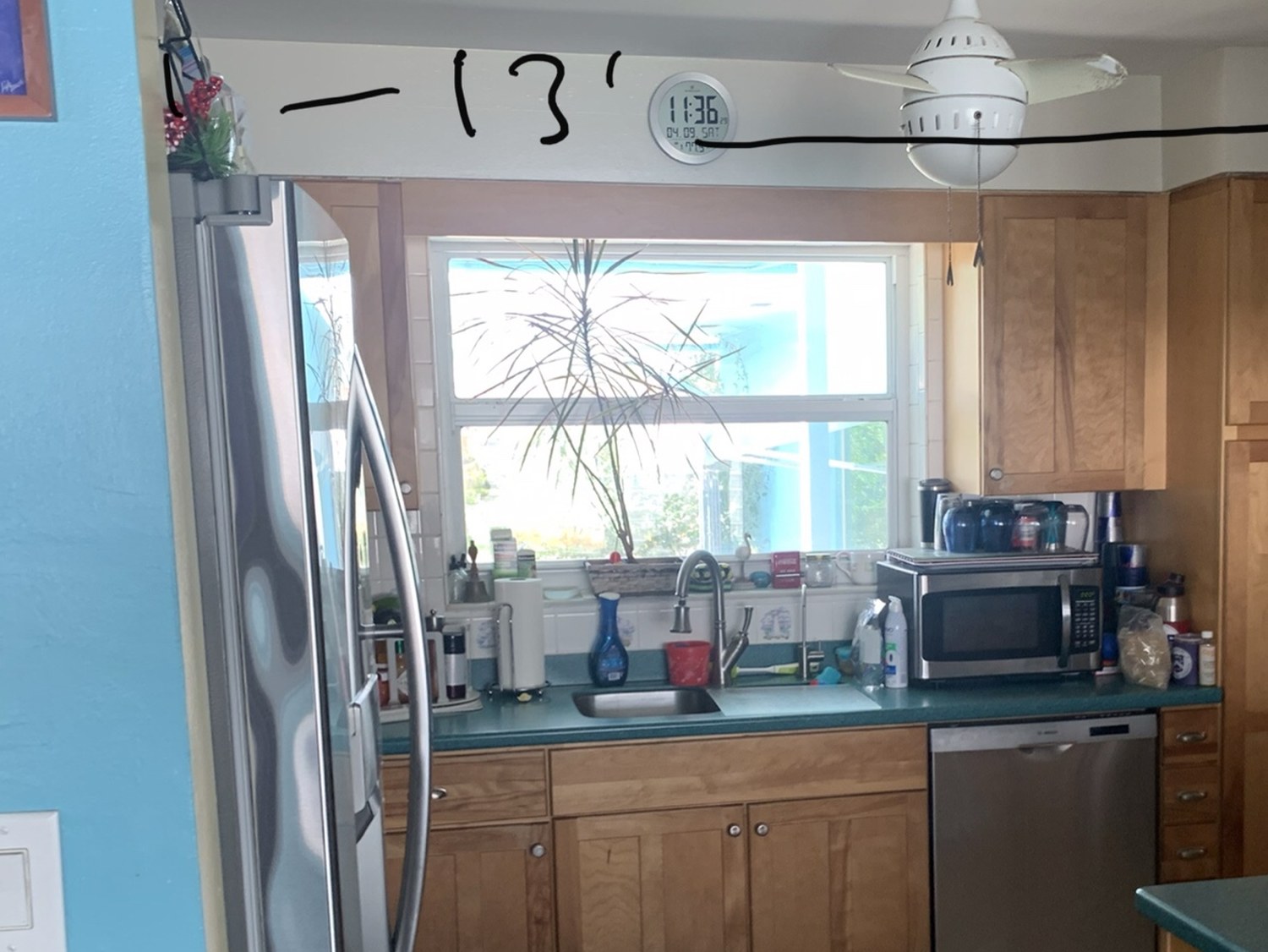 The existing kitchen before work began, with oak cabinets, a laminate counter and the room width written on the wall