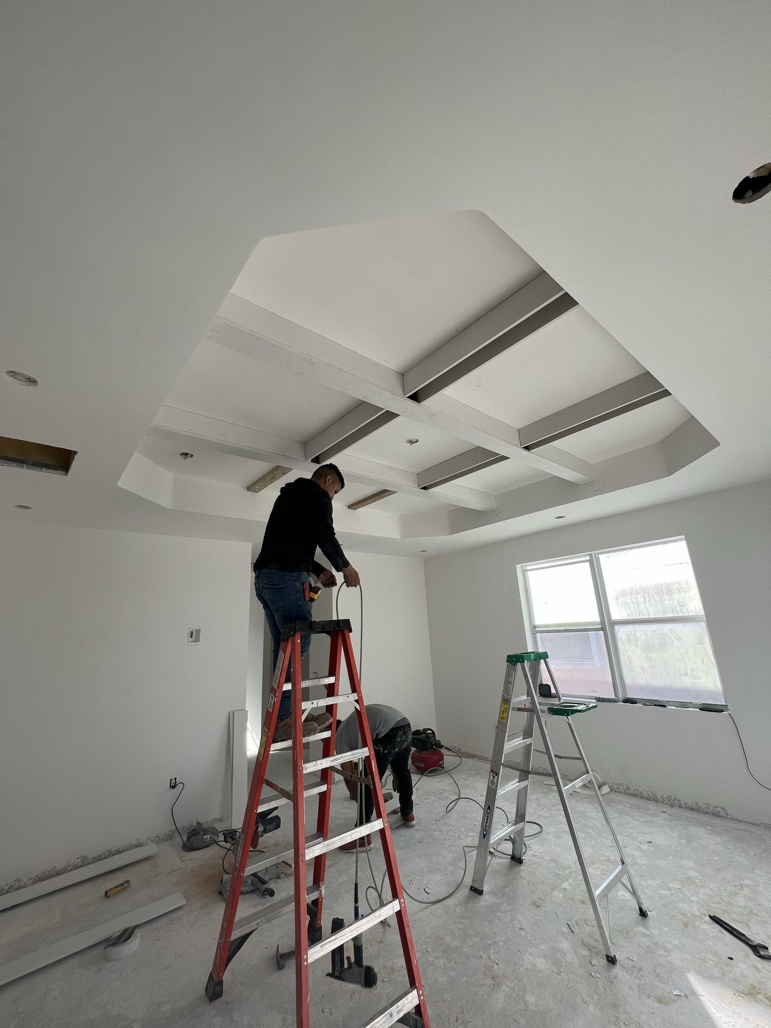 The same coffered ceiling drywalled and finished, with a crew member working from a ladder below