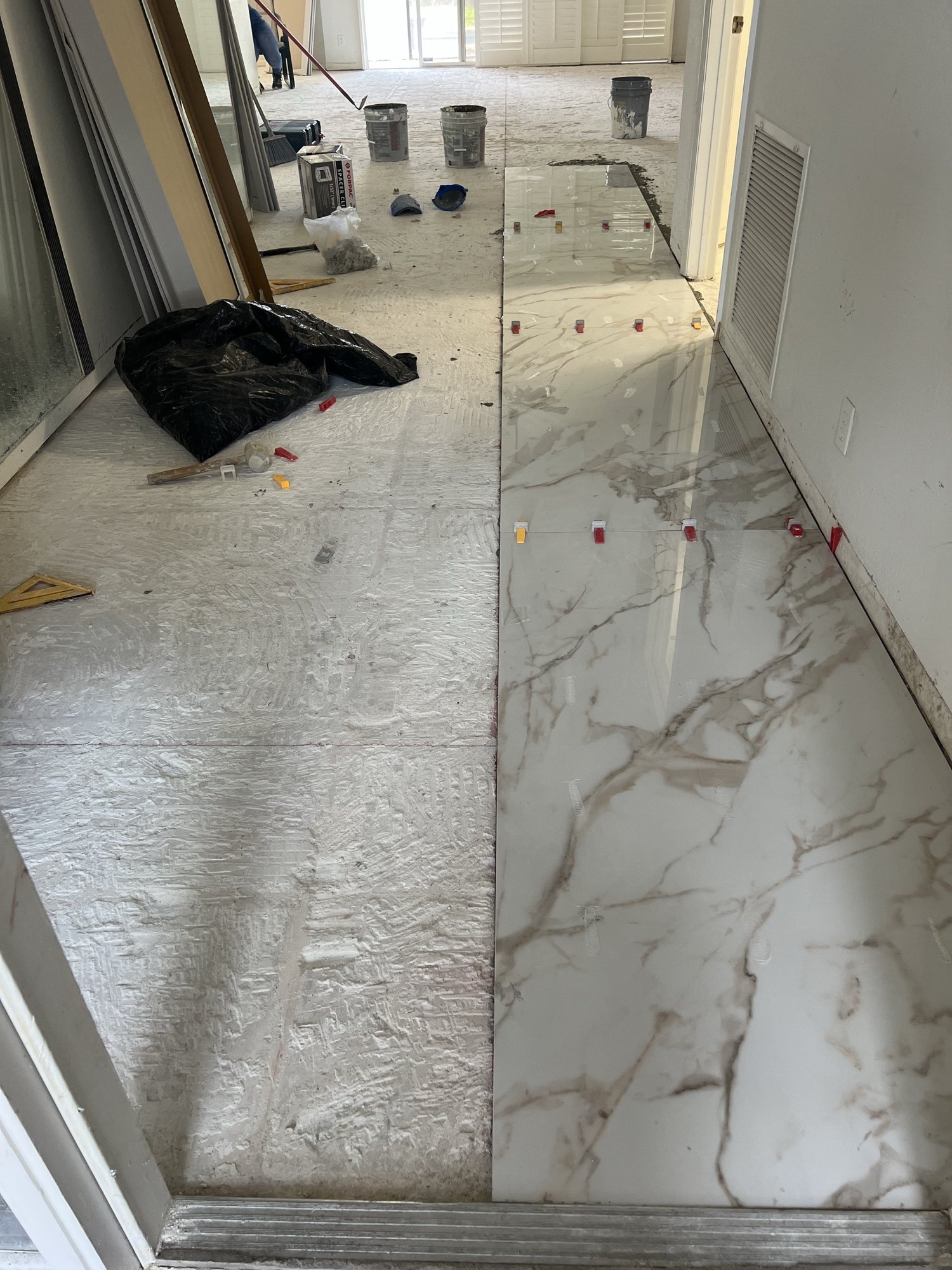 Large-format marble-look porcelain tile being set with levelling clips across a living area floor