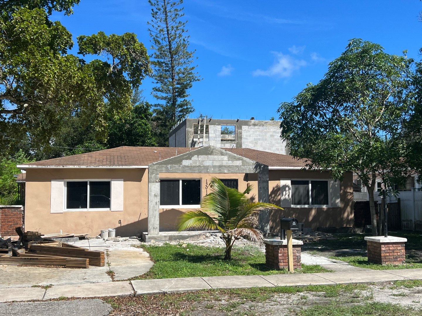 Front elevation with the new concrete block structure rising behind the original single-story house